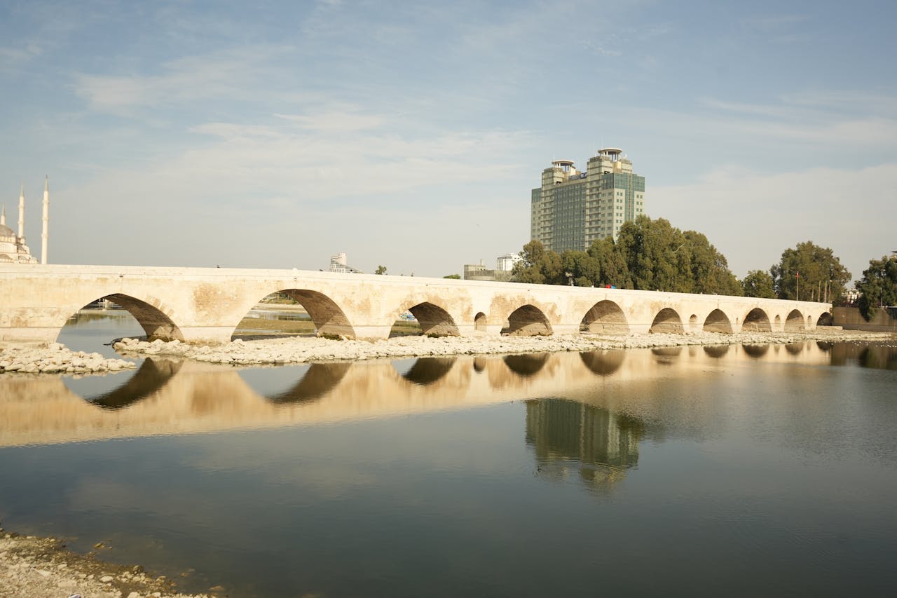 Reflection of the historic stone bridge over Seyhan River in Adana under a clear sky.