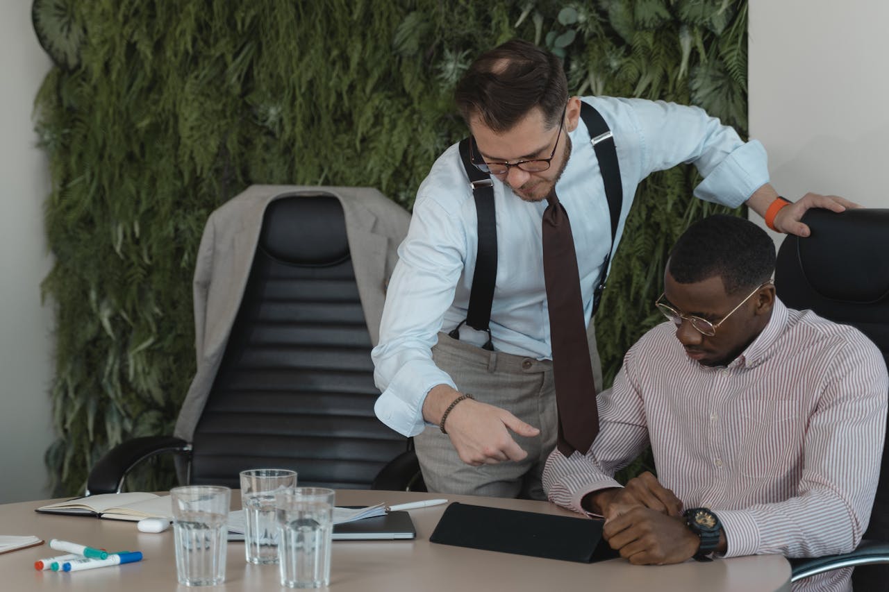 Two businessmen engaged in a collaborative office discussion, using a tablet.
