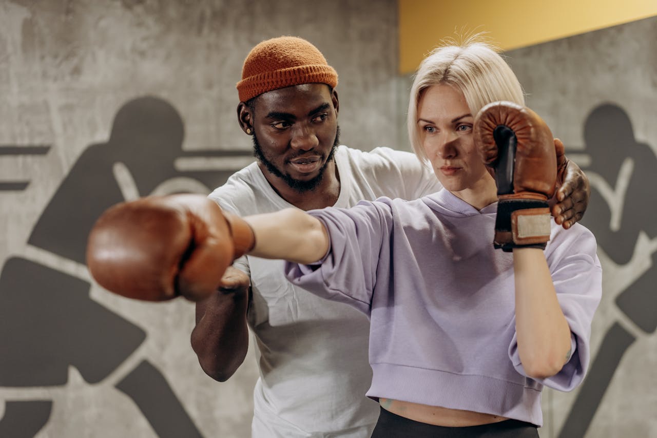A trainer guides a boxer's punching technique during an indoor gym session.